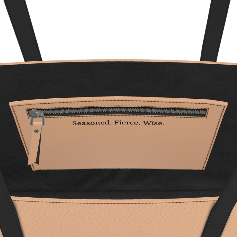 Close-up of a black and beige small tote bag with text 'Seasoned. Fierce. Wise.'